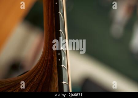 Un primo colpo del collo di una chitarra acustica in legno con archi in bronzo con messa a fuoco sulla tastiera, tasti e marcatori di posizione. Foto Stock