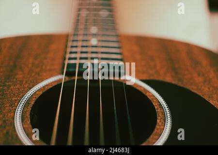 Un basso angolo di ripresa di una chitarra acustica che mostra il collo con tastiera e tasti sullo sfondo con le corde in acciaio, rosetta e buco sonoro. Foto Stock