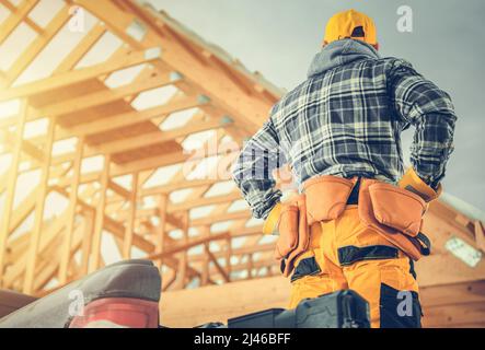 Lavoratore caucasico di costruzione di fronte al nuovo telaio di scheletro di legno sviluppato di una casa. Carpenteria tema. Foto Stock