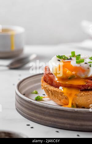 Pane tostato con uova in camicia, prosciutto e cipolla per cucinare l'uovo di benedetto su sfondo bianco. Brunch inglese. Orientamento verticale Foto Stock