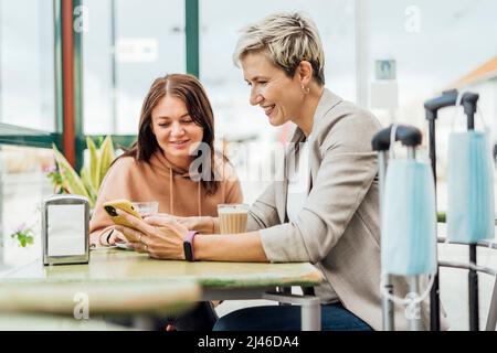 Due amiche che viaggiano in un caffè - maschera e bagagli in primo piano Foto Stock