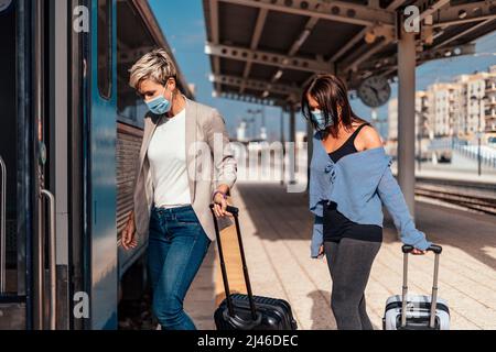 Due donne in maschere protettive salire sul treno con i bagagli Foto Stock