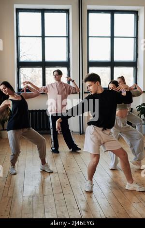 Gruppo di ragazzi adolescenti e ragazze in abbigliamento sportivo che eseguono la danza del voga in studio loft, mentre ripetono l'esercizio dopo il loro leader Foto Stock