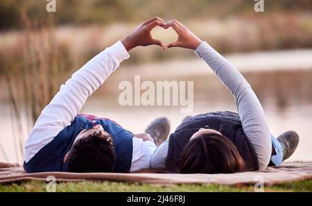 Lascia dormire sotto le stelle. Scatto di una giovane coppia che fa un segno di cuore mentre si stesa all'esterno. Foto Stock