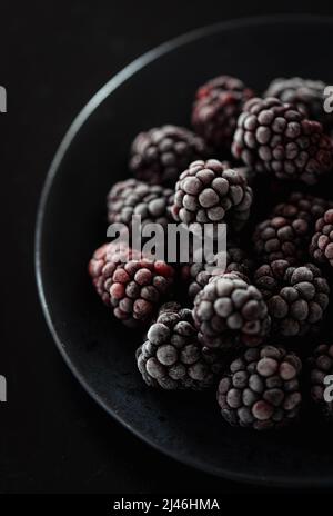 Primo piano di una ciotola nera di more congelate. Foto Stock