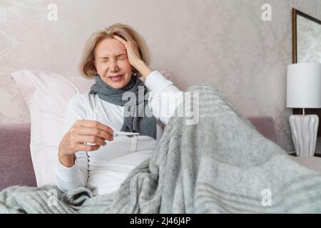 La donna soffre di un mal di testa e tiene un termometro. Foto Stock