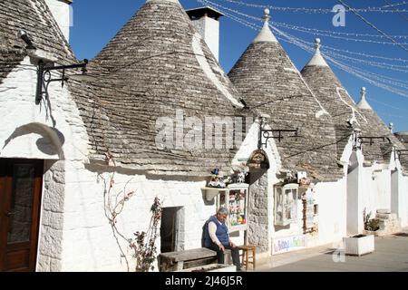 Alberobello, Italia. Il proprietario di un negozio di souvenir attende i clienti all'esterno di una tradizionale casa di trullo, risalente a 500 anni fa. Foto Stock