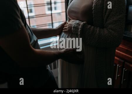 Moglie incinta in cucina con il marito che tocca il ventre Foto Stock