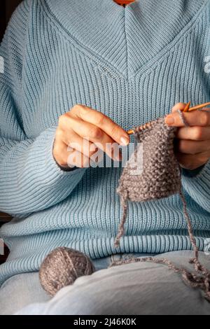 una donna di 50 anni si siede su un divano, a casa, e si unisce una sciarpa w Foto Stock