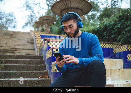 Uomo etnico in cuffie che naviga smartphone sulla scala Foto Stock