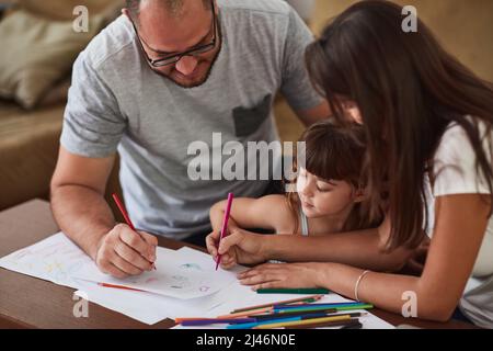 Incoraggiano il gioco creativo a casa loro. Fucilato di una madre e di un padre che si disegnano insieme alla loro figlia giovane a casa. Foto Stock