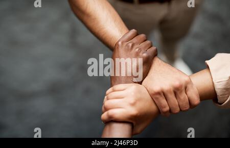 Tenere sulla vostra fame per il successo. Colpo di un gruppo di uomini d'affari che collegano le armi in solidarietà in un ufficio moderno. Foto Stock