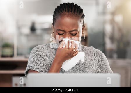 E improvvisamente è stata la stagione influenzale. Scatto di una giovane donna d'affari che soffia il naso e usa un laptop in un ufficio moderno. Foto Stock