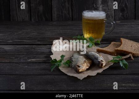 pesce vobla salato e secco con birra ambrata su sfondo di legno scuro con pane sul tavolo, con spazio copia Foto Stock