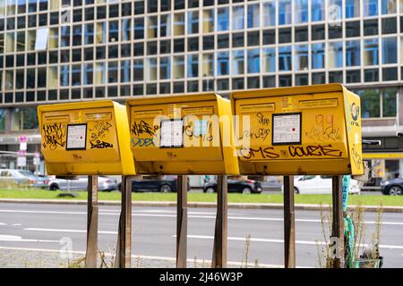 Tre caselle postali gialle della Deutsche Post accanto a una grande strada della città. Mailbox per inviare lettere e biglietti. Etichette e adesivi Graffiti. Foto Stock