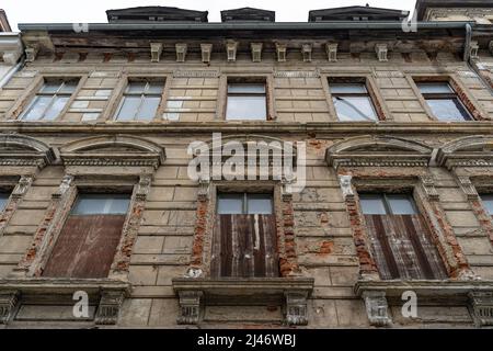 Facciata di una vecchia casa abbandonata. Guardando fino al gocciolatoio del tetto. Architettura di un edificio storico con intemperie. Vetro rotto delle finestre. Foto Stock