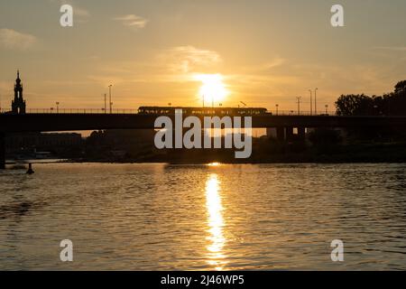 Un tram passa su un ponte di fronte al luminoso sole serale. Silhouette di una funivia come trasporto pubblico. Tramonto in una città della Sassonia. Foto Stock