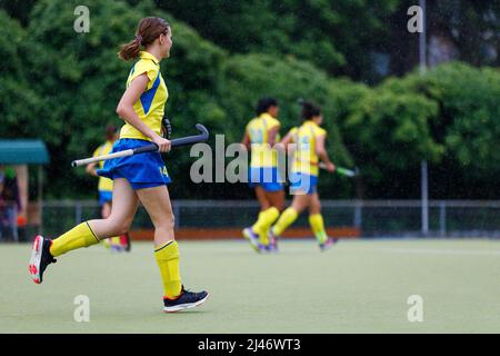 Giovane ragazza adolescente che corre in campo durante la partita di hockey su campo in pioggia Foto Stock