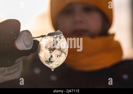 una ragazza tiene una bolla di sapone con bei modelli di gelo nei raggi del sole in inverno Foto Stock