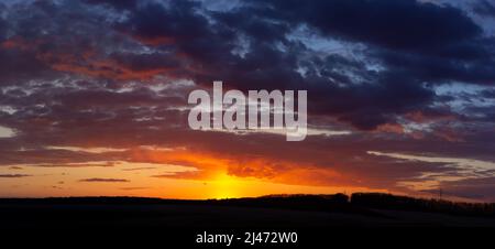 Panorama di tramonto, nuvole blu e sole rosso illumina le nuvole in oro Foto Stock