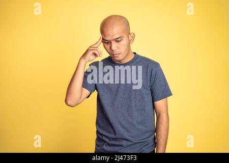 l'uomo calvo asiatico che pensa duro con il dito che punta alla fronte Foto Stock