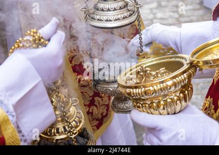 Un ragazzo altare o un'accolita in una processione della settimana Santa che riempe uno dei censori di incenso Foto Stock