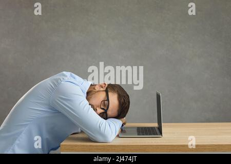 Studente stanco o lavoratore d'ufficio che dorme seduto alla scrivania vicino al computer portatile Foto Stock