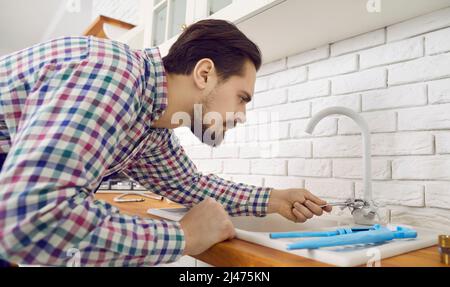 Il giovane idraulico o il riparatore sta fissando o installando un rubinetto del miscelatore nella cucina Foto Stock