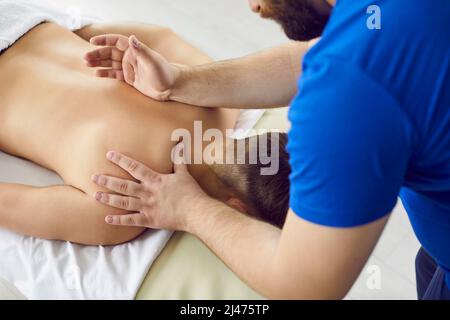 Massagista professionista presso il centro benessere o la sala massaggi che effettua un massaggio alla schiena per il giovane uomo Foto Stock