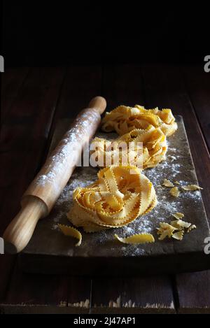Cucina italiana. Pappardelle di pasta fatta in casa e spilla di laminazione isolata su sfondo ligneo. Direttamente sopra. Foto Stock