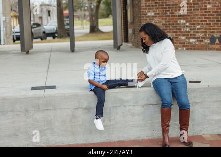 Una mamma che aiuta suo figlio legando le sue scarpe mentre fuori Foto Stock