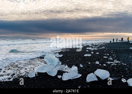 Pezzi di ghiaccio e iceberg rotti su una spiaggia di sabbia nera vulcanica al tramonto (Diamond Beach, Islanda) Foto Stock