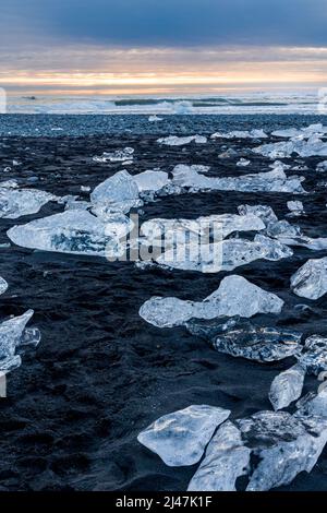 Pezzi di ghiaccio e iceberg rotti su una spiaggia di sabbia nera vulcanica al tramonto (Diamond Beach, Islanda) Foto Stock