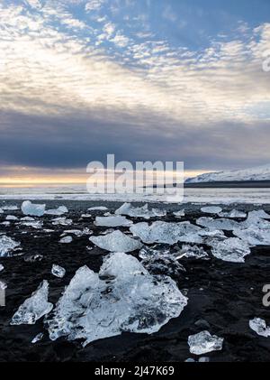 Pezzi di ghiaccio e iceberg rotti su una spiaggia di sabbia nera vulcanica al tramonto (Diamond Beach, Islanda) Foto Stock