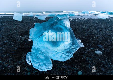 Pezzi di ghiaccio e iceberg rotti su una spiaggia di sabbia nera vulcanica al tramonto (Diamond Beach, Islanda) Foto Stock