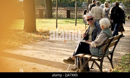 Coppia caucasica anziana seduta sul banco nel parco, marito disabile in occhiali e un bastone Park selettivo fuoco pieno scatto copia spazio . Foto di alta qualità Foto Stock