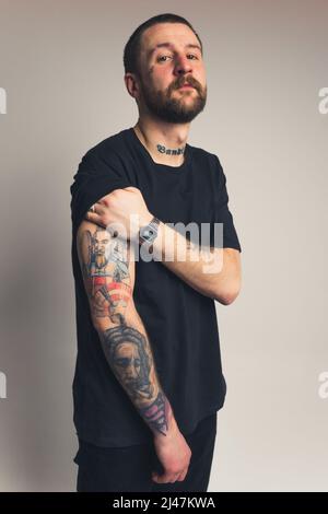 Giovane uomo europeo sicuro con baffi da barba e tatuaggi che guardano criticamente cowboy shot studio shot gradiente sfondo verticale. Foto di alta qualità Foto Stock