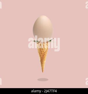 Concetto sul tema di Pasqua 2022, uovo come simbolo della vacanza in un cono gelato su sfondo rosa con un'ombra, cartolina. Foto Stock