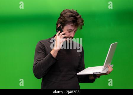 uomo che parla al telefono tenendo il laptop sullo schermo verde Foto Stock