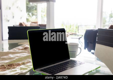 Primo piano di un computer portatile con schermo nero e una tazza di caffè sul tavolo da pranzo in una casa Foto Stock