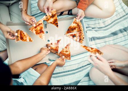 Tempo di Chow. Shot di amici irriconoscibili che condividono la pizza all'aperto. Foto Stock