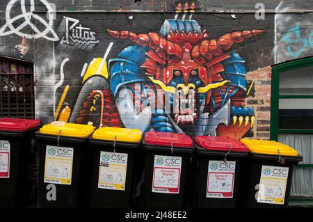 Street art murale giustapposto con bidoni dei rifiuti urbani (rifiuti), codificati a colori per il riciclaggio, in AC/DC Lane, Melbourne, Australia Foto Stock