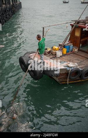 Una piccola spazzatura tradizionale è usata per rimuovere i rifiuti galleggianti dal porto di Victoria vicino ai moli dei traghetti centrali, Hong Kong, 2007 Foto Stock