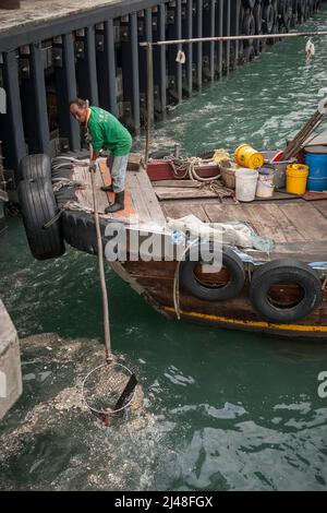 Una piccola spazzatura tradizionale è usata per rimuovere i rifiuti galleggianti dal porto di Victoria vicino ai moli dei traghetti centrali, Hong Kong, 2007 Foto Stock