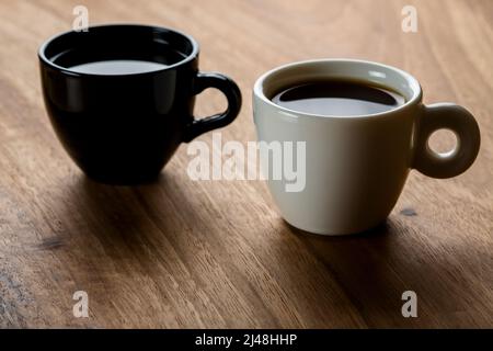 Due tazze di caffè in bianco e nero su sfondo di legno Foto Stock