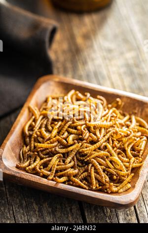 Vermi salati fritti. Vermi arrosto in una ciotola su tavola di legno. Foto Stock