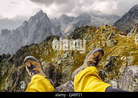 Escursionista seduto sulla collina e guardando sulle montagne. Scarpe da trekking sulle gambe di turisti. Escursioni in Tatra alta in Slovacchia Foto Stock