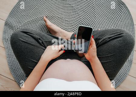 Donna incinta con un telefono in mano, vista dall'alto. Concetto di shopping online. Foto Stock