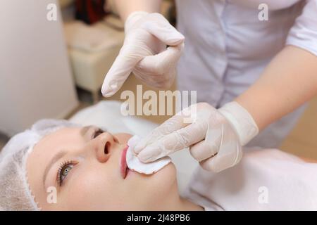 L'estetista tiene una goccia di olio sulle sue dita dopo l'iniezione di acido ialuronico di fronte alle labbra della ragazza Foto Stock