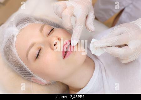 L'estetista macchia l'olio sulle labbra della ragazza dopo la procedura di iniezione dell'acido ialuronico Foto Stock